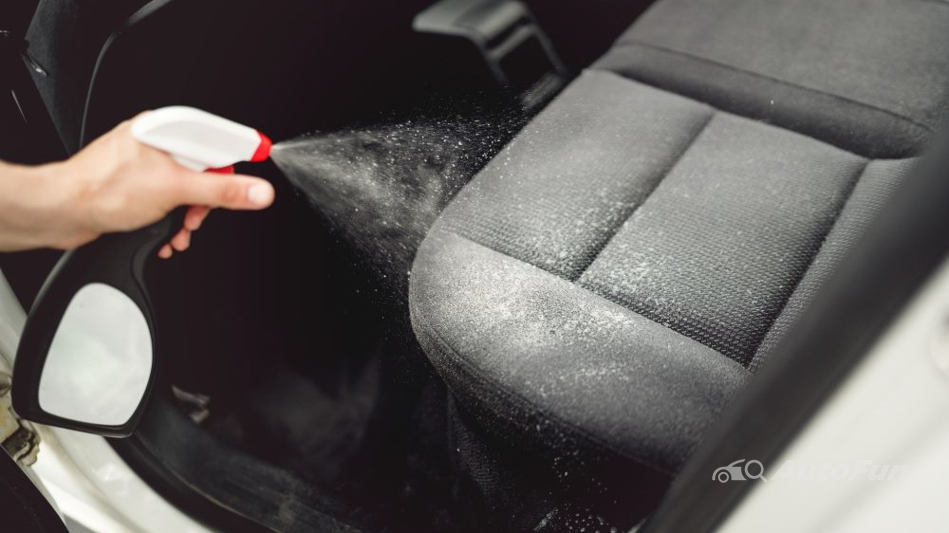 close shot of a hand with spray bottle spraying mold removal solution on car seat